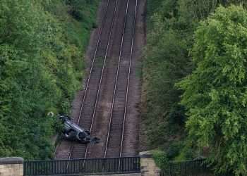 Man in his 70s dies after car falls down embankment and crashes onto train tracks as busy rail route closed 