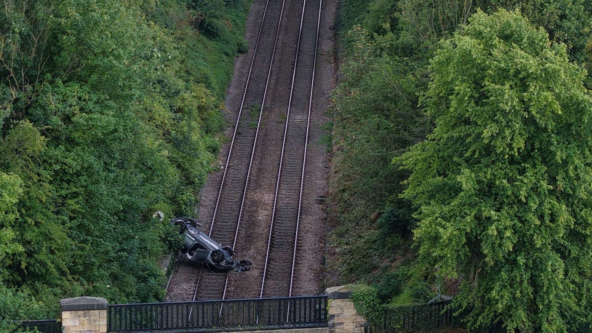 Man in his 70s dies after car falls down embankment and crashes onto train tracks as busy rail route closed 